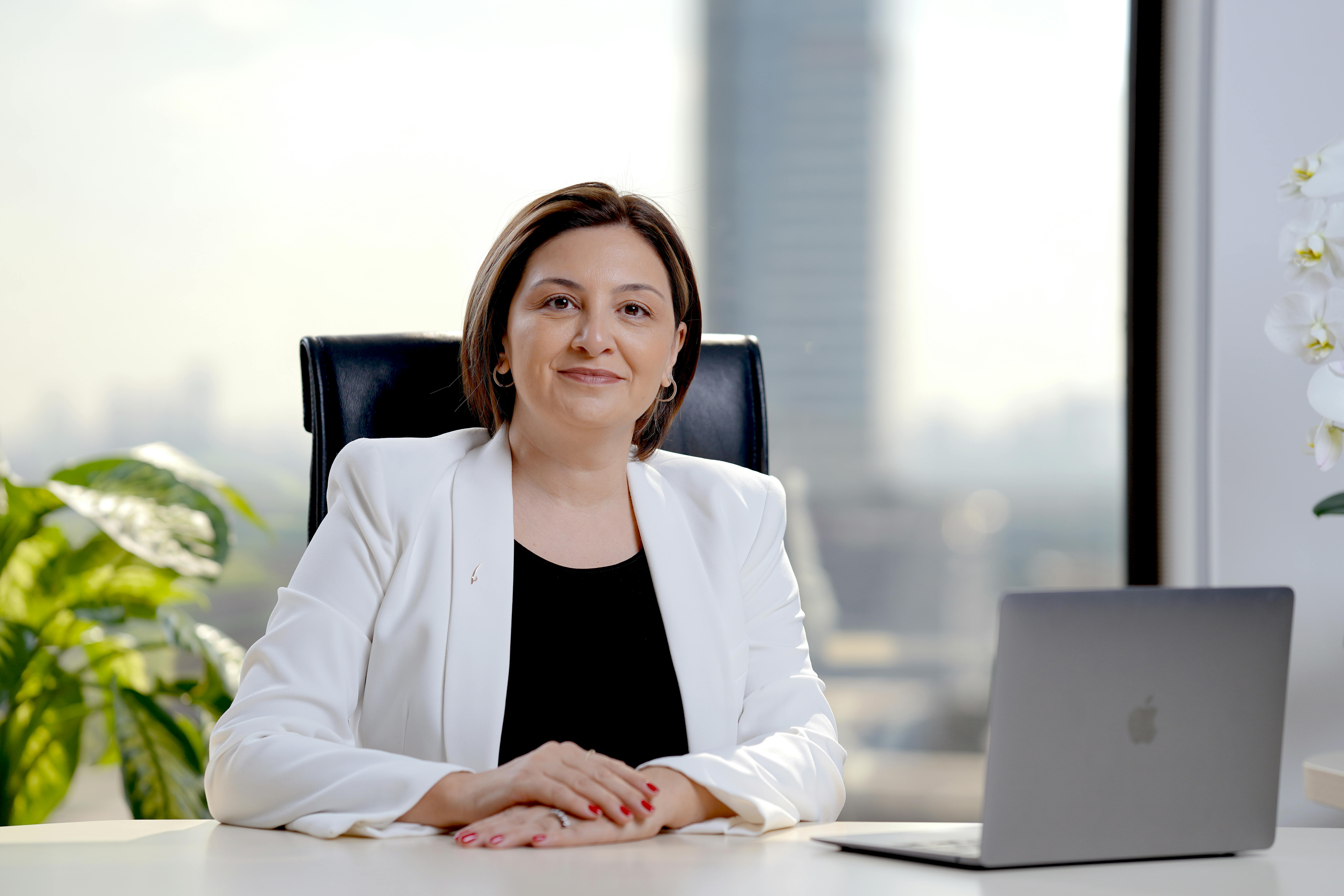 Professional woman in office, smiling and sitting at desk with laptop, showcasing success.